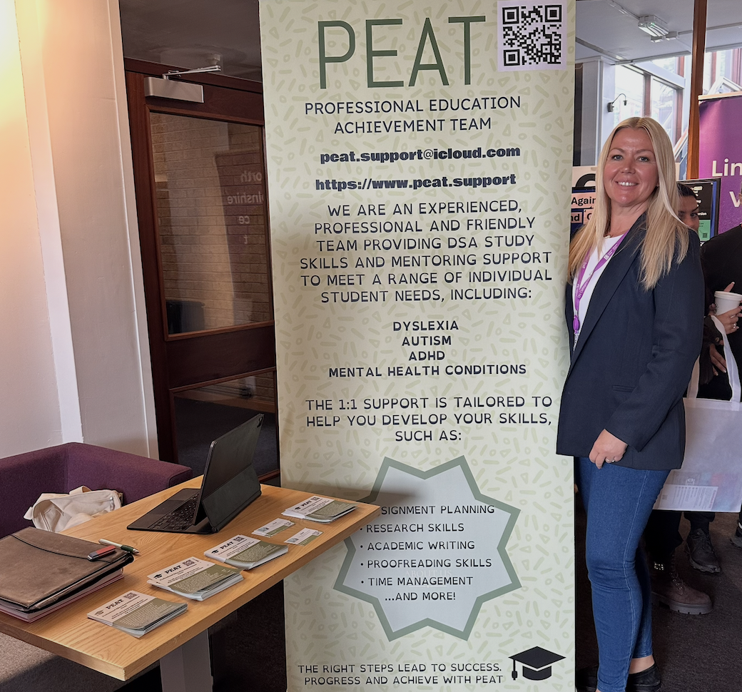 A person standing beside the PEAT support banner at an information stand